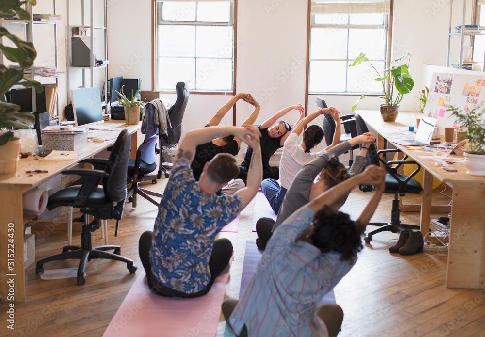 Creative business people stretching, practicing yoga in office